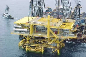 A large yellow platform in the ocean with cranes.