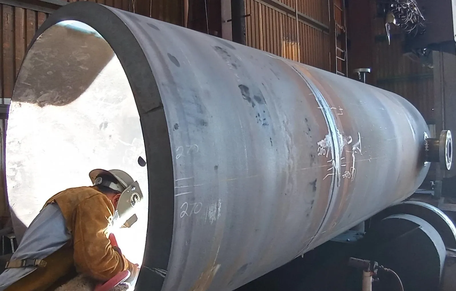 A man working on a large pipe in an industrial setting.