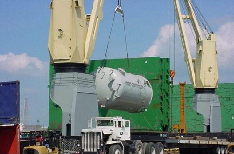 Crane lifting large cylindrical industrial tank onto truck